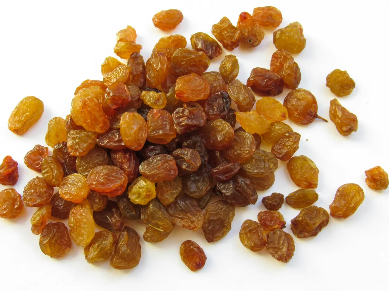 A pile of golden and brown raisins on a white surface